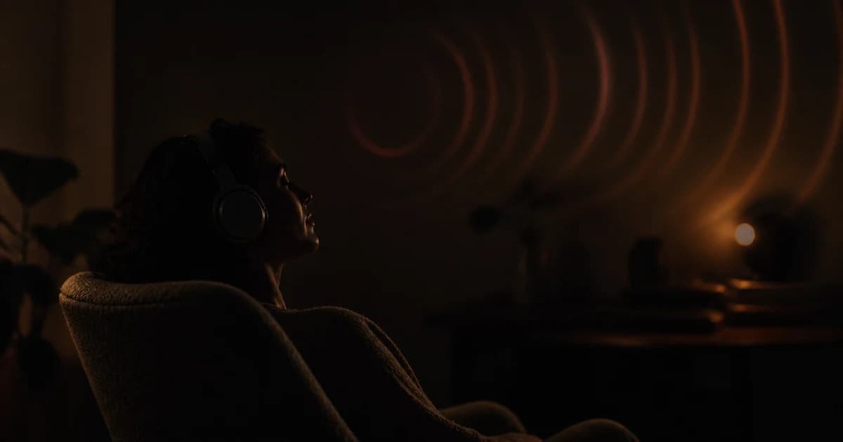 An adult in a dark room resting in a chair with headphones and eyes closed